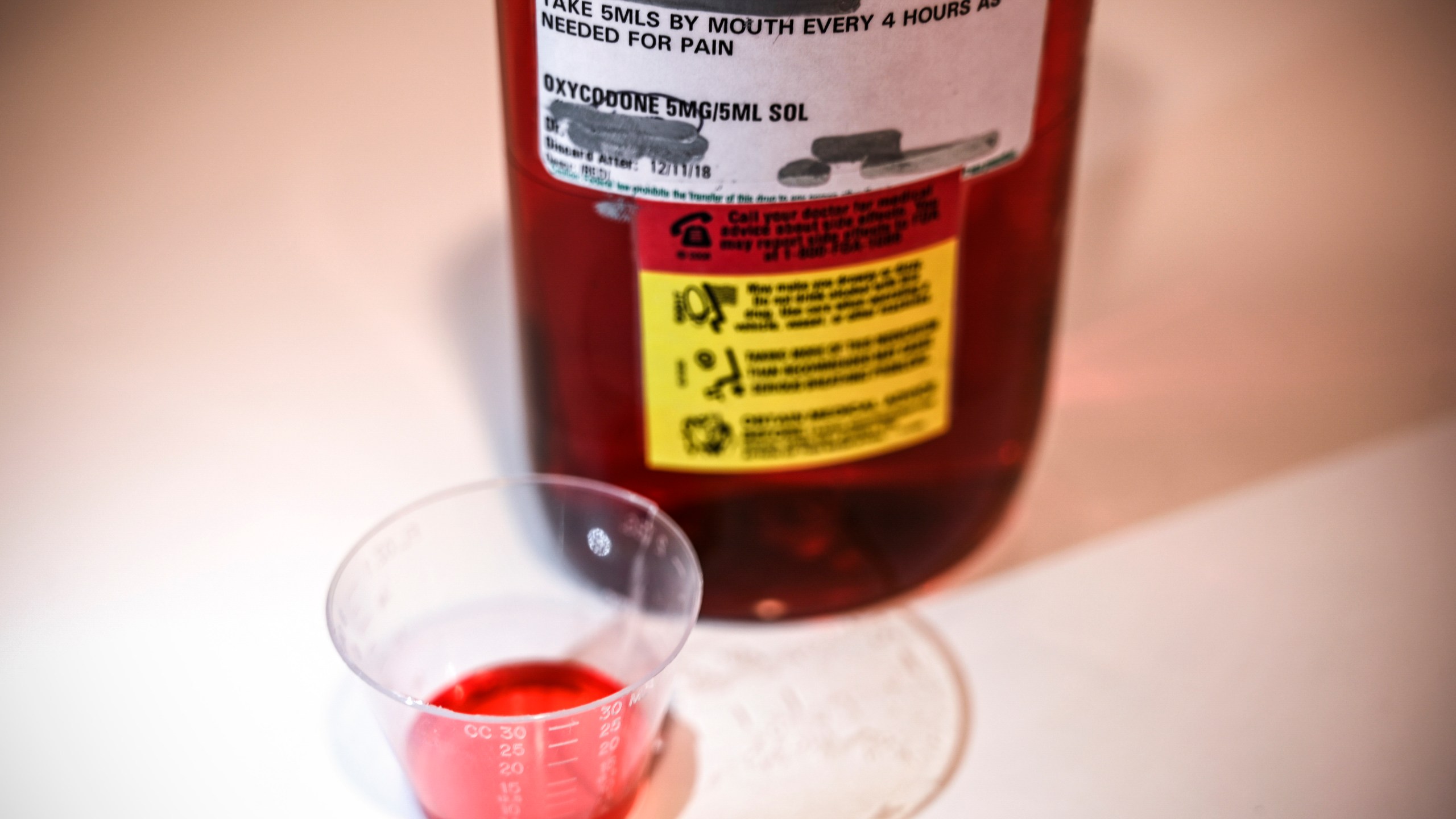 A 500ml bottle of liquid oxycodone, an opioid pain relief medication, and a dose of 5ml of the solution sit on a table in Washington, D.C., March 29, 2019. (Credit: EVA HAMBACH/AFP/Getty Images)