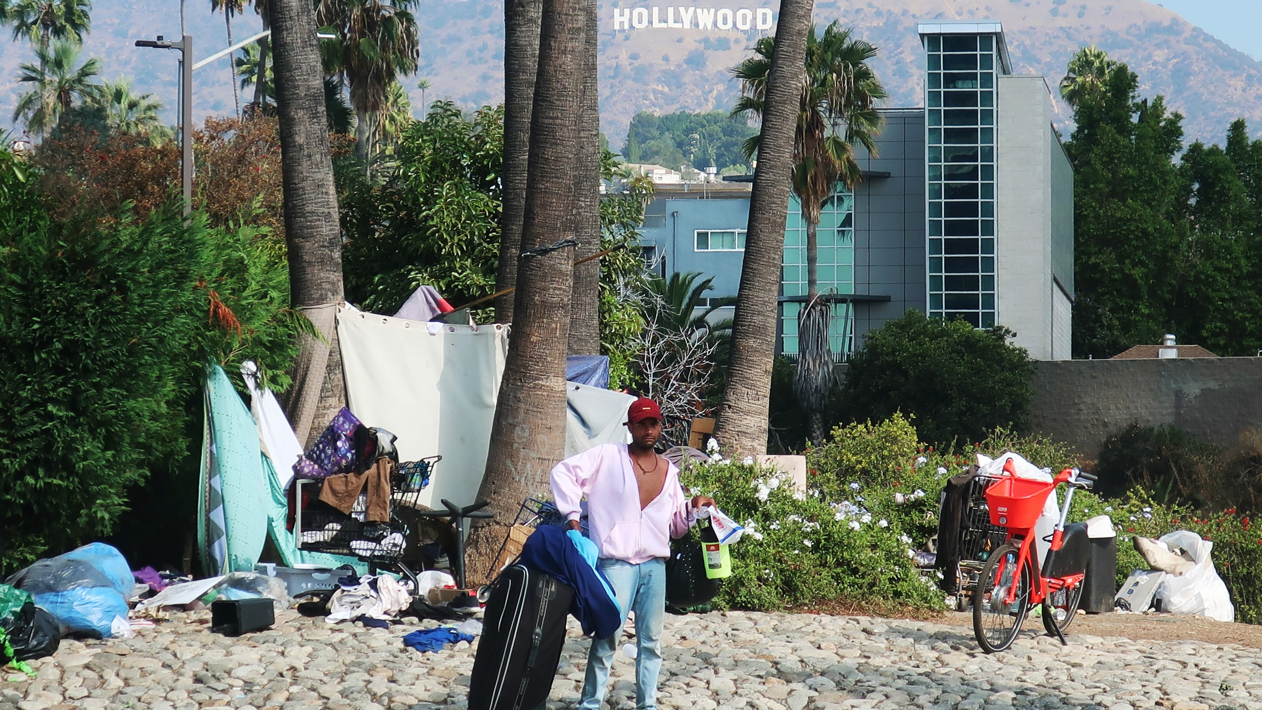 A man stands in front of a homeless encampment in Los Angeles, with the Hollywood sign in the background on Sept. 23, 2019. (Credit: Mario Tama/Getty Images)