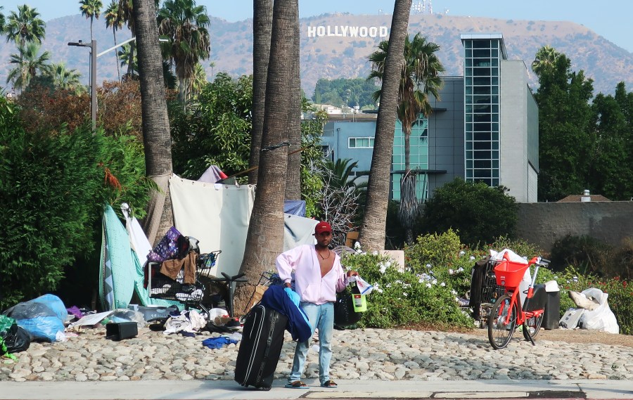 A man stands in front of a homeless encampment in Los Angeles, with the Hollywood sign in the background on Sept. 23, 2019. (Credit: Mario Tama/Getty Images)