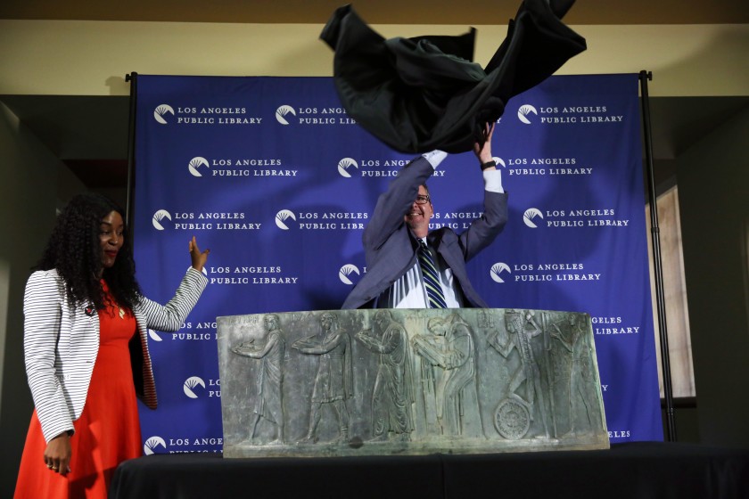 The director of the Los Angeles Central Library, Kren Malone, left, watches as City Librarian John F. Szabo unveils the recovered piece of the long-lost Well of the Scribes sculpture on Oct. 4, 2019.(Credit: Dania Maxwell/Los Angeles Times)