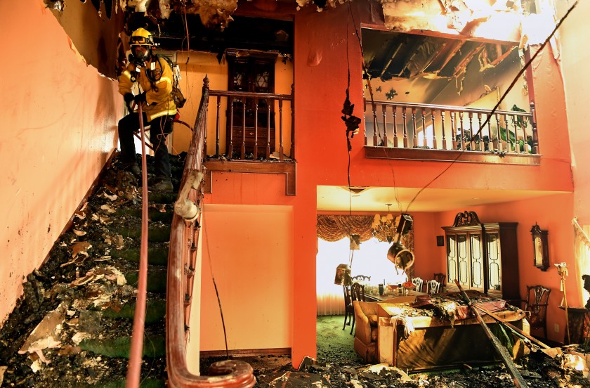 An Orange County firefighter pulls hose into a damaged house after the Saddleridge Fire burned along Beaufait Avenue in Porter Ranch on Oct. 11, 2019. (Credit: Wally Skalij / Los Angeles Times)