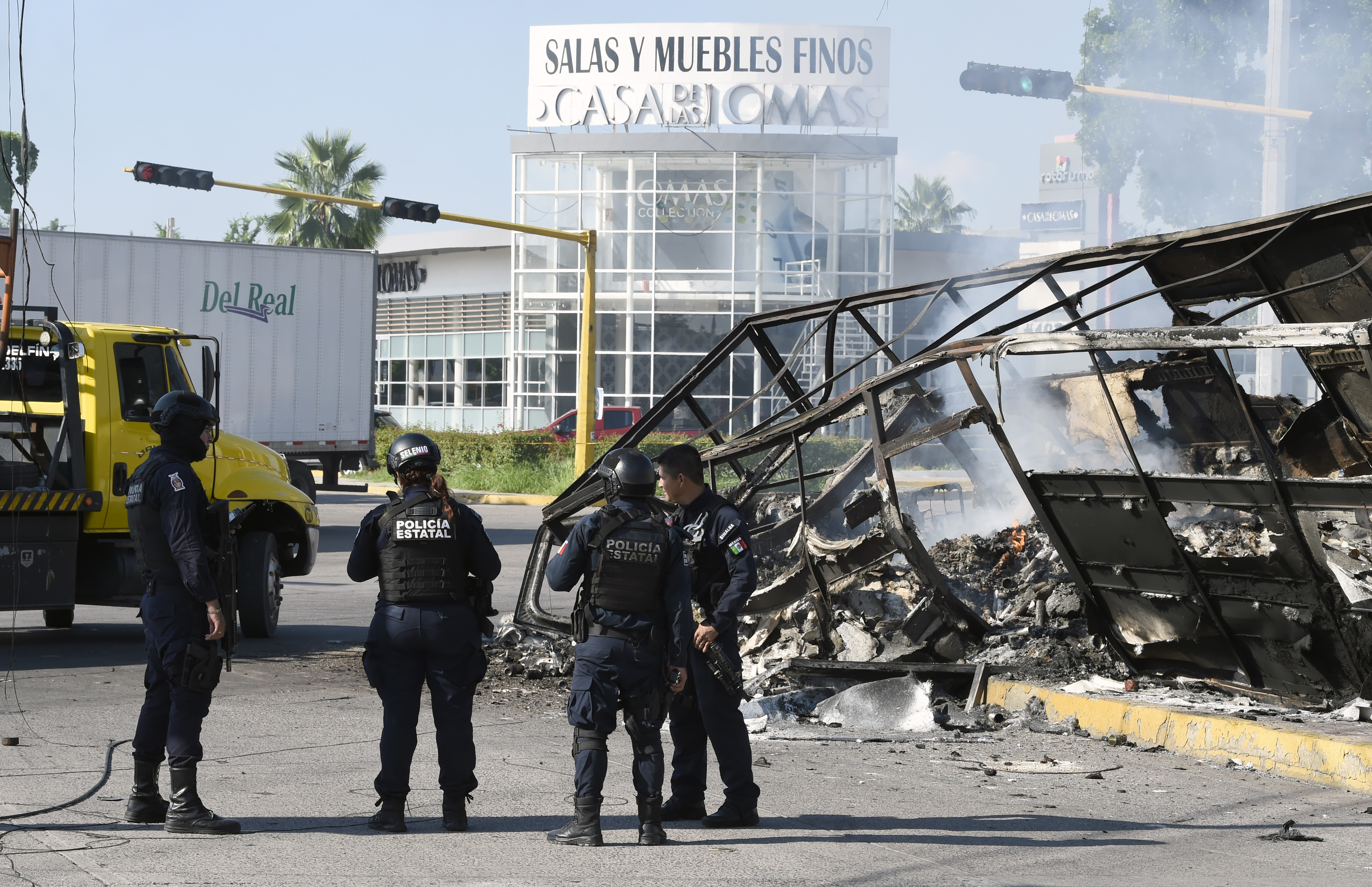 Policemen stand next to a burnt vehicle after heavily armed gunmen waged an all-out battle against Mexican security forces in Culiacan, Sinaloa state, Mexico, on Oct. 18, 2019. (Credit: ALFREDO ESTRELLA / AFP/Getty Images)