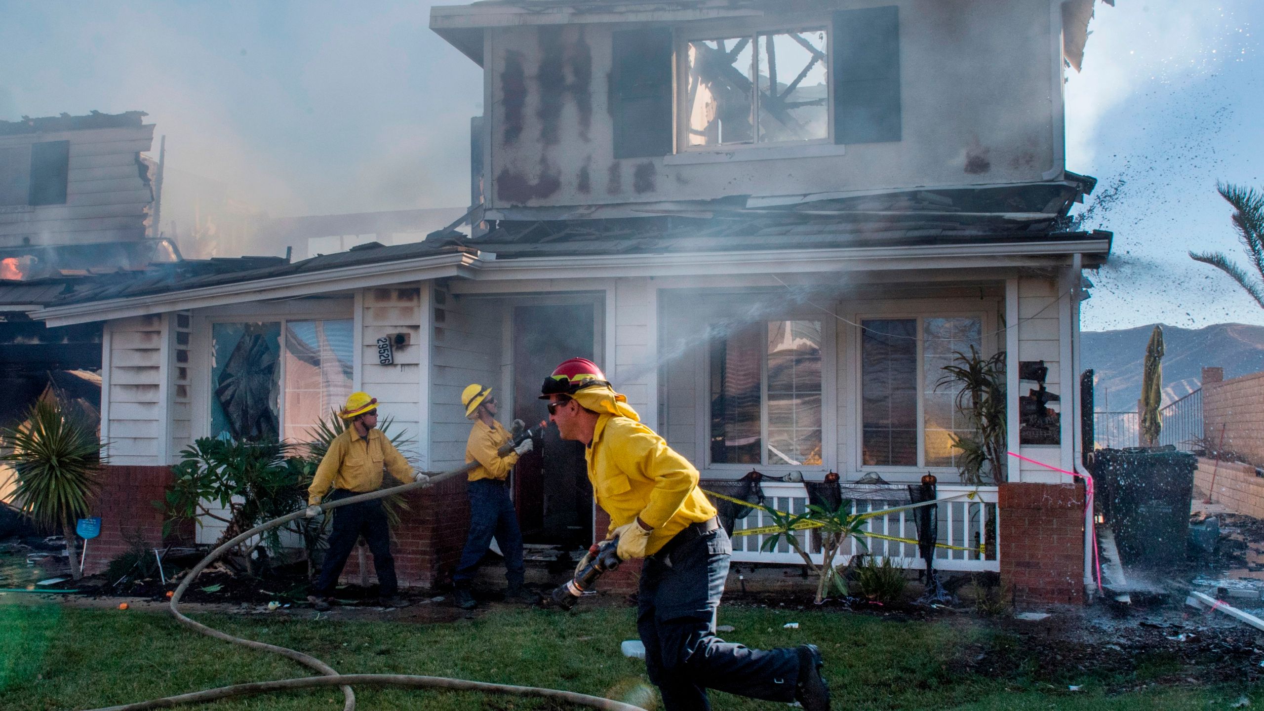 Firefighters hose down a burning house during the Tick Fire in Agua Dulce near Santa Clarita, California on Oct. 25, 2019. (Credit: MARK RALSTON/AFP via Getty Images)