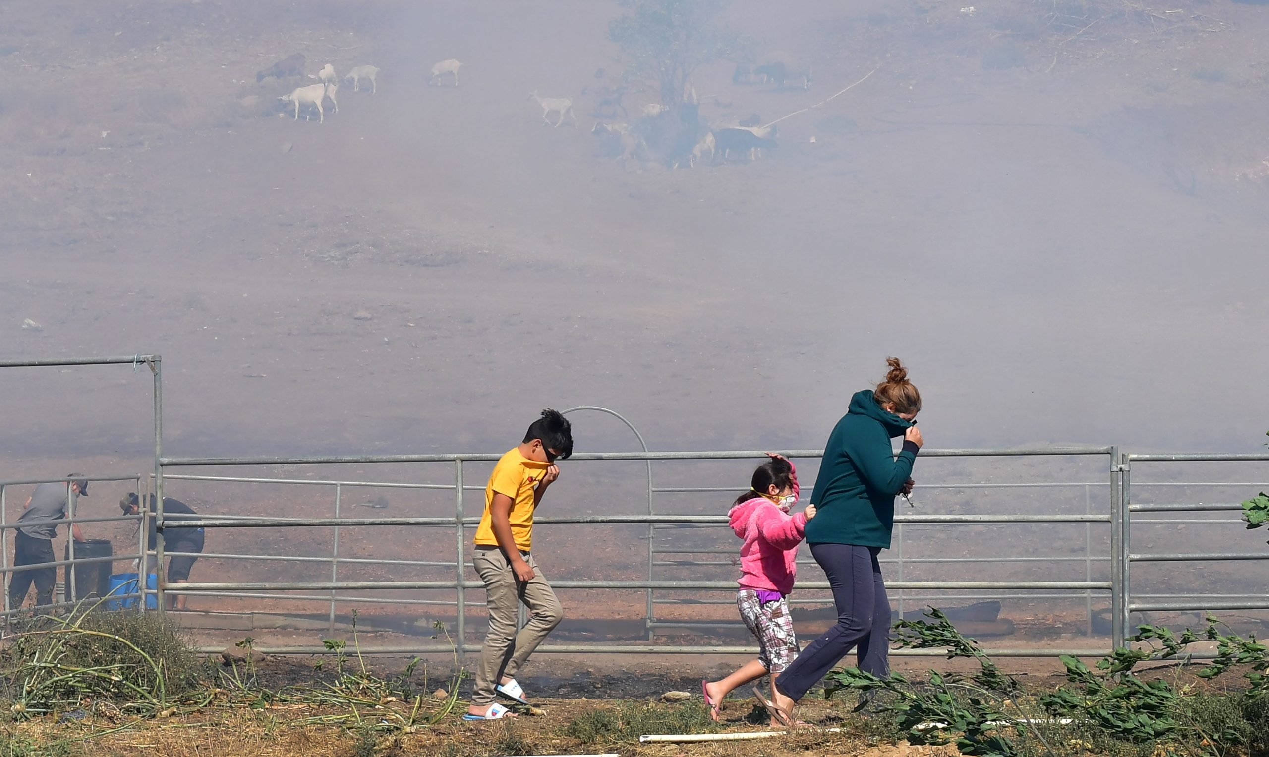 A woman and children brace themselves from strong winds and smoke near the Ronald Reagan Presidential Library in Simi Valley during the Easy Fire. (Credit: FREDERIC J. BROWN/AFP via Getty Images)