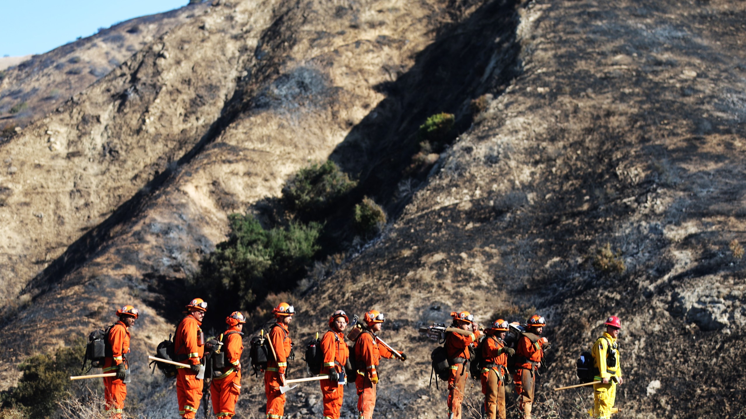 An inmate firefighter crew from Prado Conservation Camp, led by a fire captain (R), prepare to put out hot spots from the Saddleridge Fire on Oct. 12, 2019, in Porter Ranch, California. (Credit: Mario Tama/Getty Images)