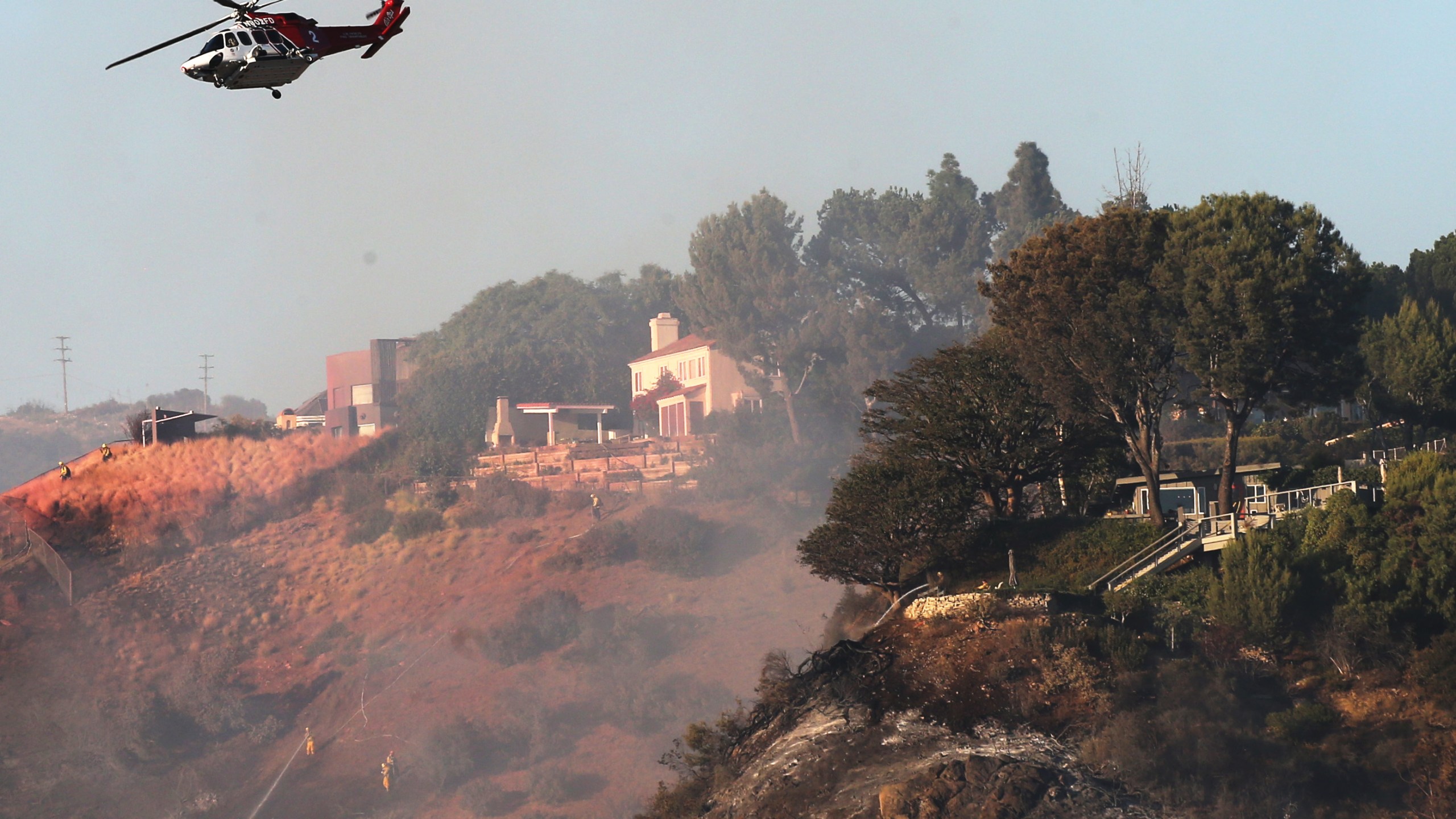 A firefighting helicopter flies near homes during the Palisades Fire in Pacific Palisades on Oct. 21, 2019. (Credit: Mario Tama / Getty Images)