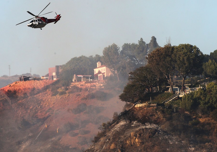 A firefighting helicopter flies near homes during the Palisades Fire in Pacific Palisades on Oct. 21, 2019. (Credit: Mario Tama / Getty Images)