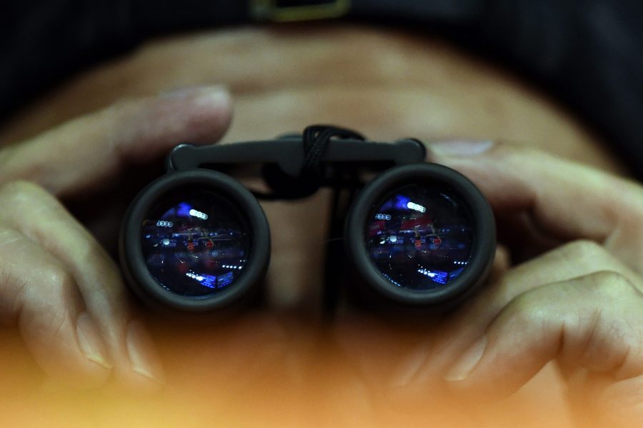 A person looks through binoculars. (Credit: JOHANNES EISELE/AFP via Getty Images)