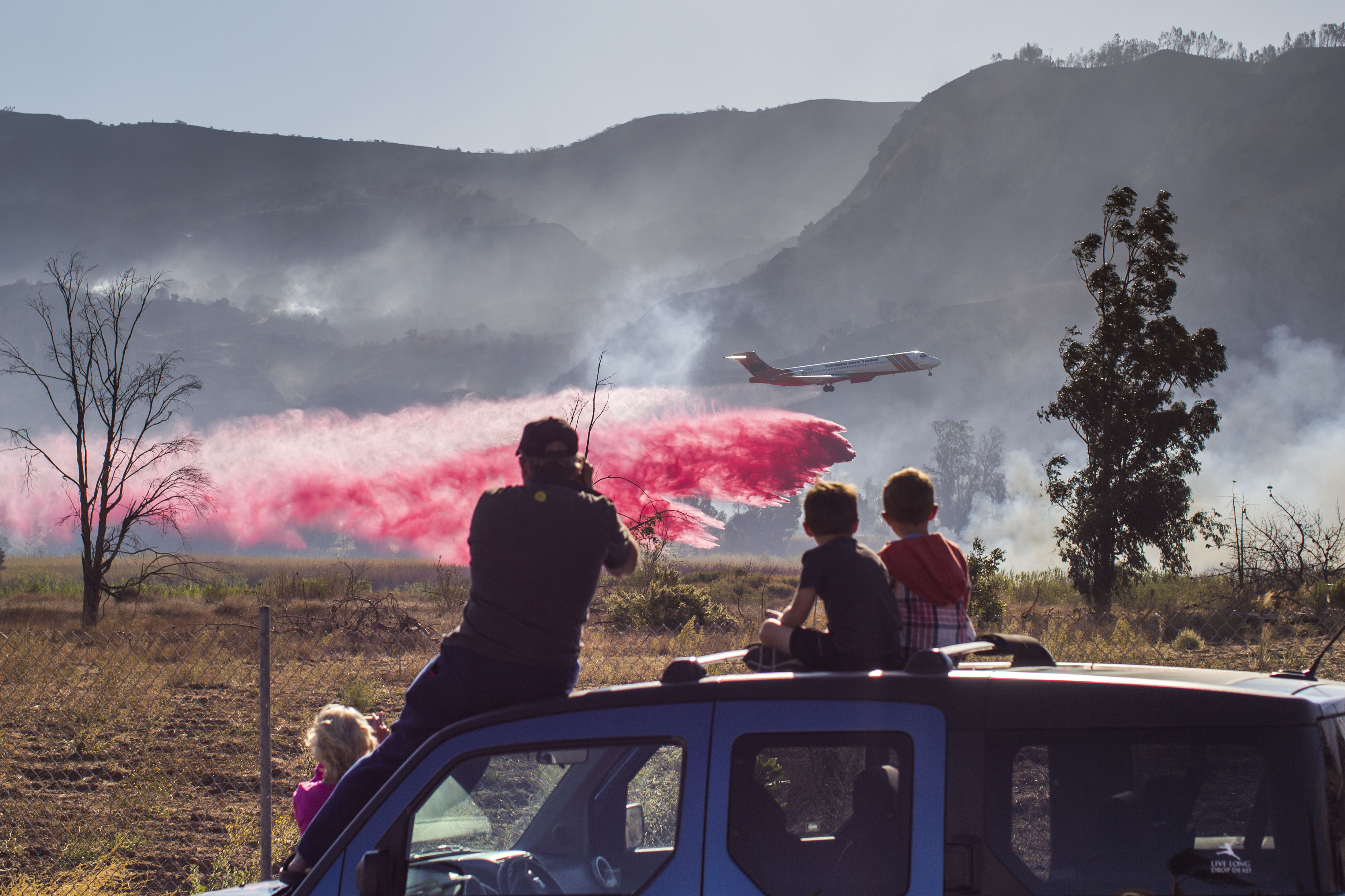 A family watches an air tanker dropping fire retardant battling the Maria Fire in Santa Paul on Nov. 1, 2019. (Credit: Apu Gomes / AFP / Getty Images)