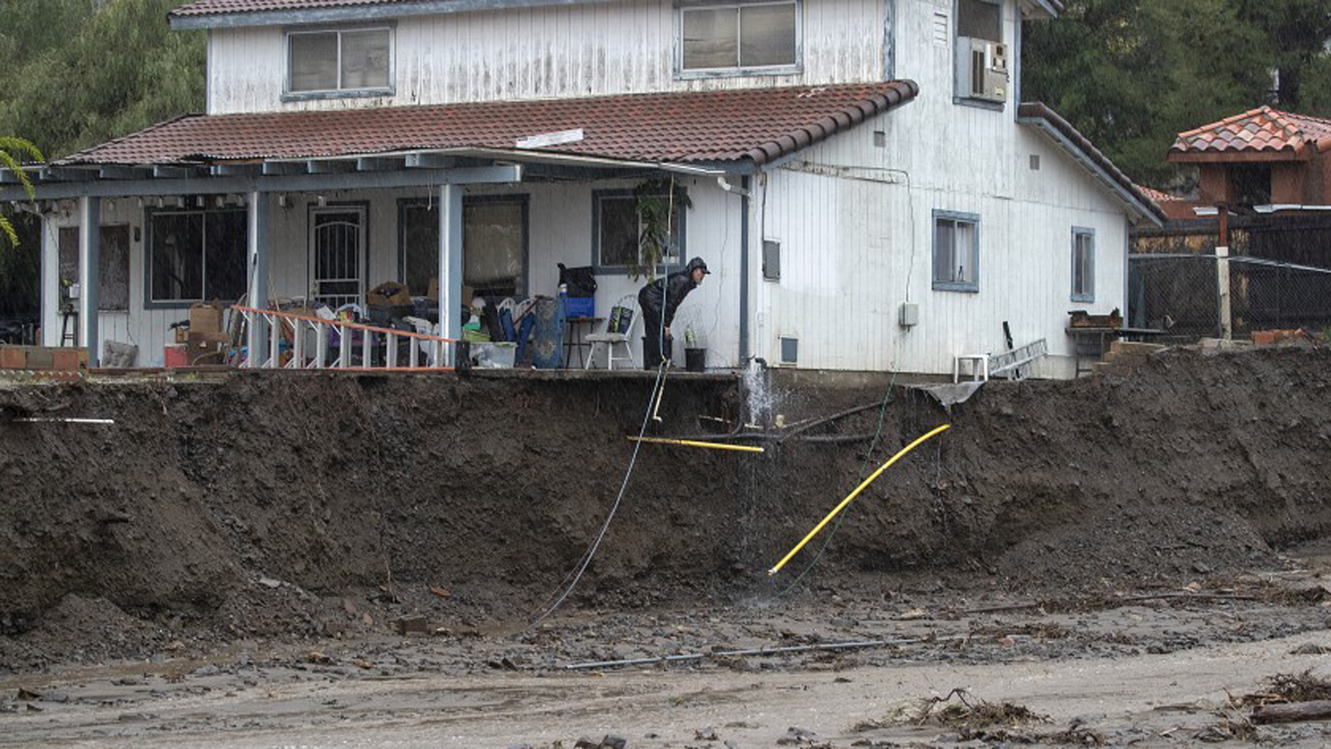 A man peers beyond the porch of his home, which was undermined by floodwater in February 2019 in Lake Elsinore’s Leach Canyon.(Credit: Allen J. Schaben / Los Angeles Times)