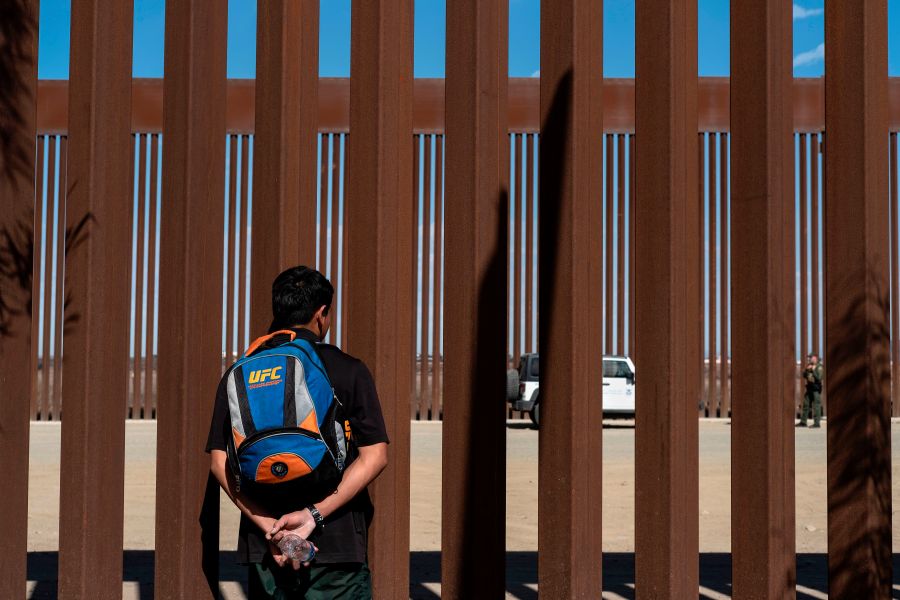 A migrant from Guatemala watches border patrol officers through the border fence at the Mexican side of the U.S.-Mexico border in Tijuana, Mexico, on Nov. 2, 2019. (Credit: Guillermo Arias/AFP via Getty Images)