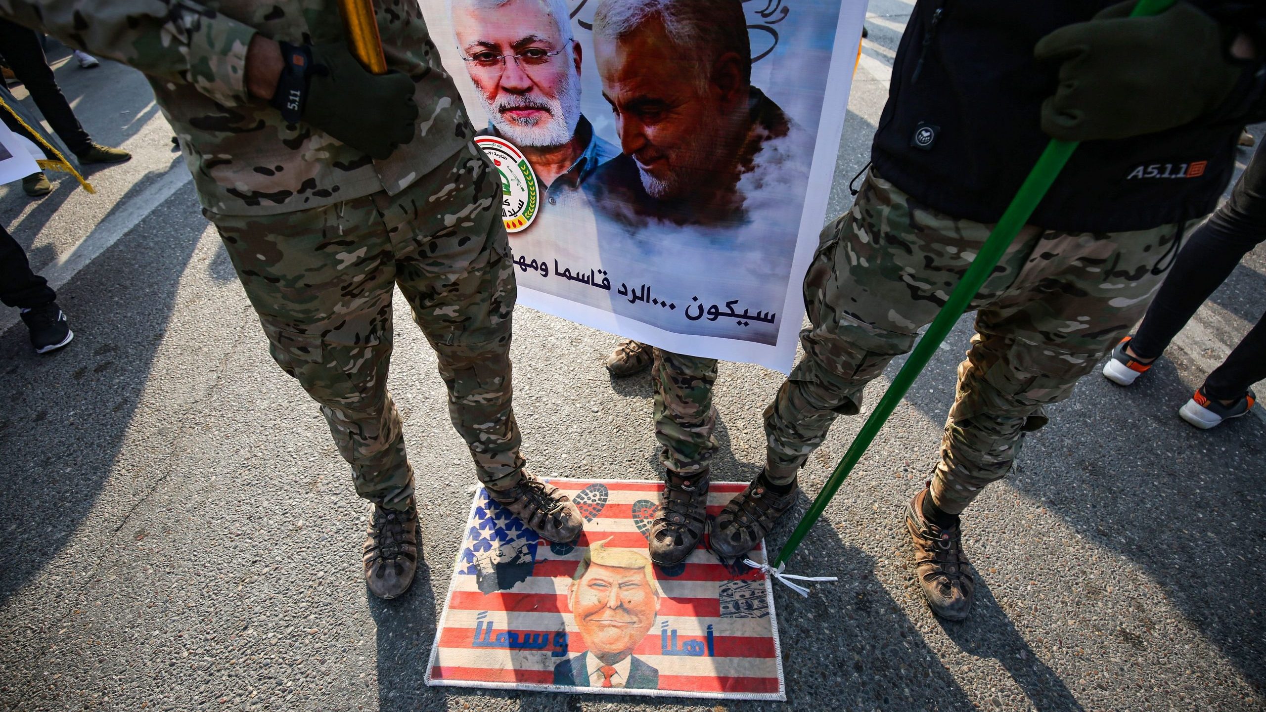 Members of the Hashed al-Shaabi paramilitary force step on a makeshift U.S. flag bearing a caricature of Donald Trump during the funeral procession of Abu Mahdi al-Muhandis, Qassem Soleimani and eight others in the capital Baghdad's district of al-Jadriya, near the high-security Green Zone, on Jan. 4, 2020. (Credit: AHMAD AL-RUBAYE/AFP via Getty Images)