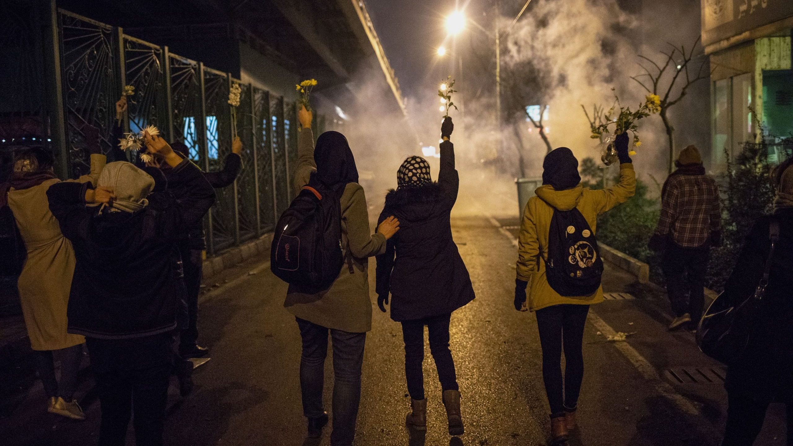 Iranian protesters hold flowers as riot police fire tear gas during a demonstration in front of Tehran's Amir Kabir University on January 11, 2020. (Credit: STR/AFP via Getty Images)