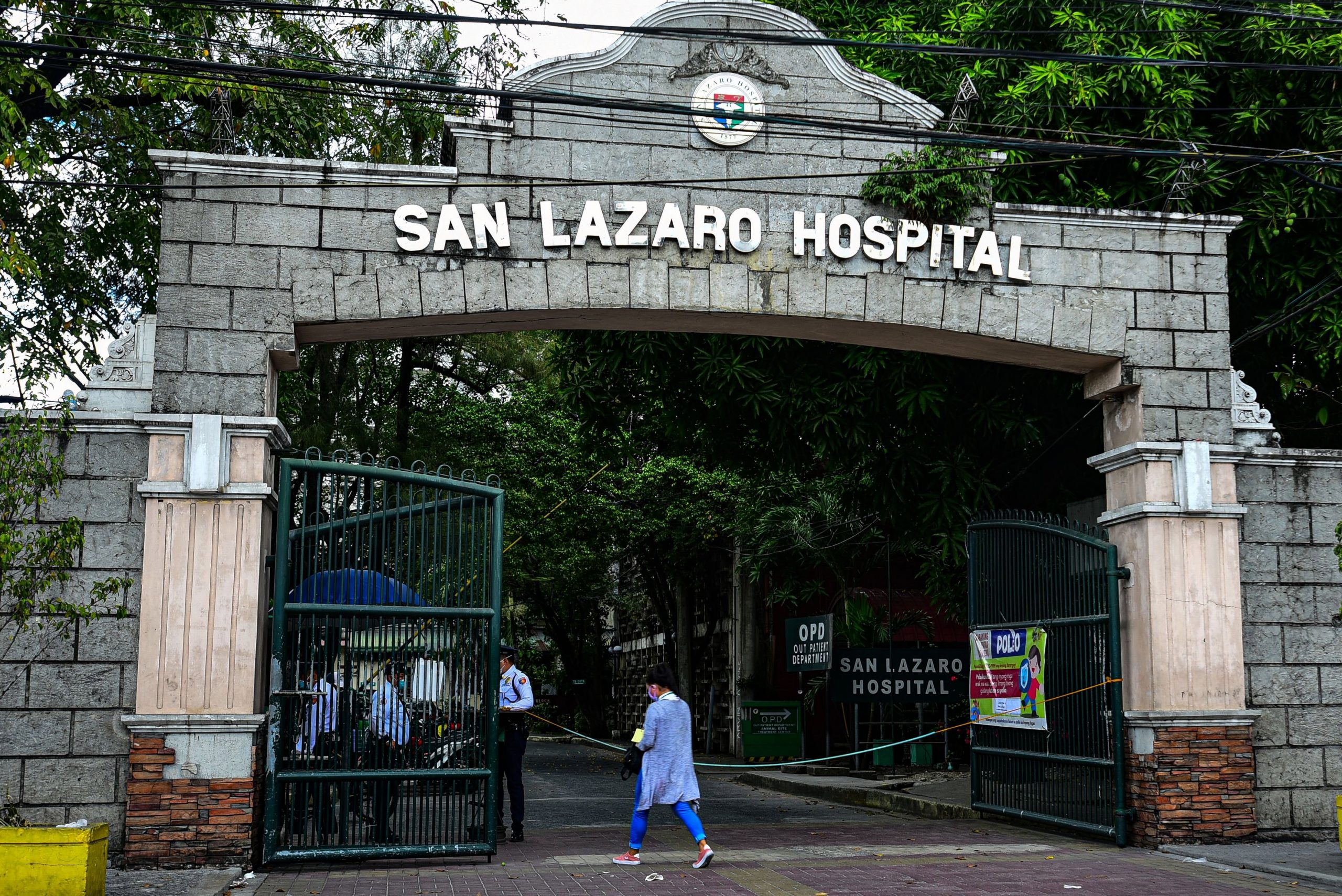 People wearing face masks walk past the main gates of the San Lazaro Hospital in Manila on Feb. 2, 2020. (Credit: MARIA TAN/AFP via Getty Images)