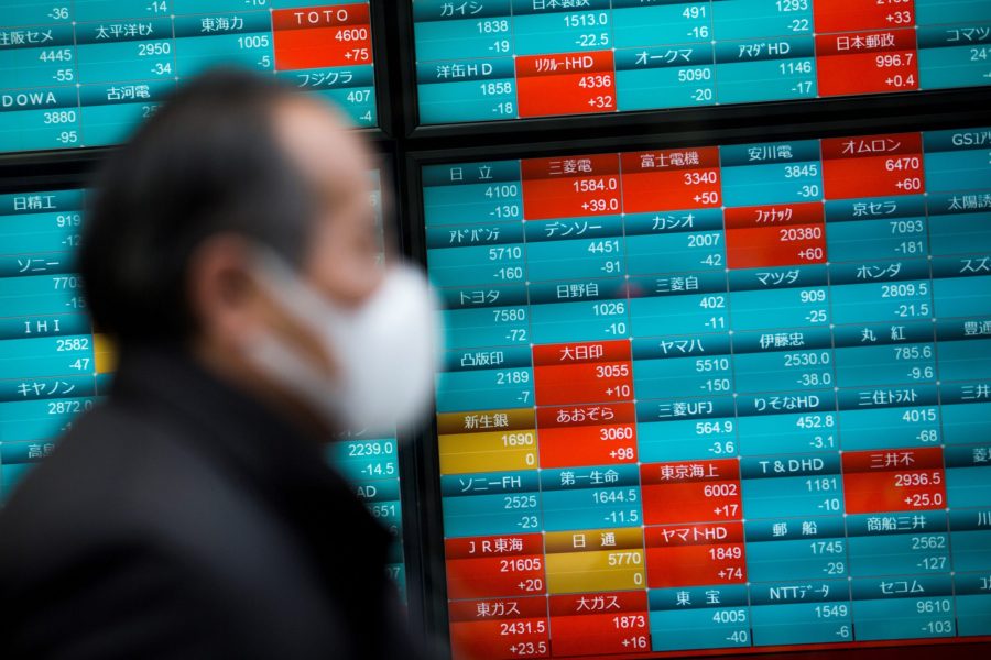 A pedestrian wearing a face mask walks past a stock indicator displaying share prices of the Tokyo Stock Exchange in Tokyo on Feb.3, 2020. (Credit: BEHROUZ MEHRI/AFP via Getty Images)