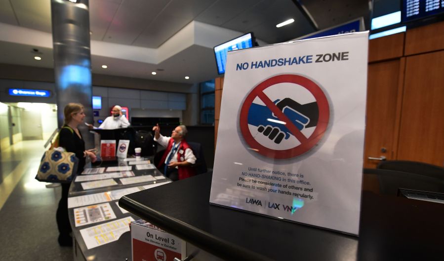 A traveler speaks to a worker at an information booth beside a reminder not to shake hands over coronavirus concerns at Los Angeles International Airport on March 12, 2020. (FREDERIC J. BROWN/AFP via Getty Images)