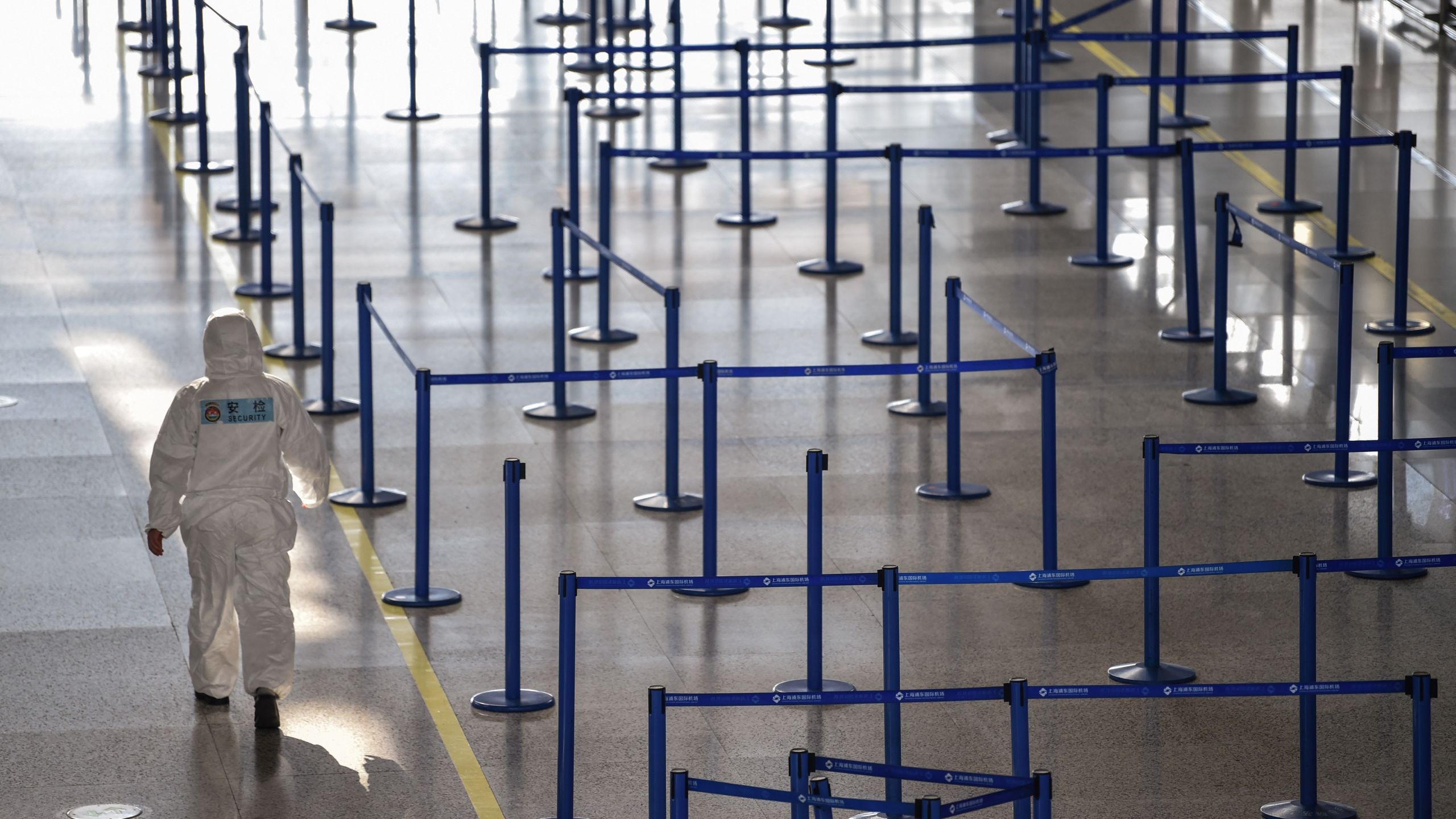 An airport security worker wearing protective gear while walking past check-in counters at Shanghai Pudong International Airport on March 18, 2020. (Hector Retamal/AFP via Getty Images)