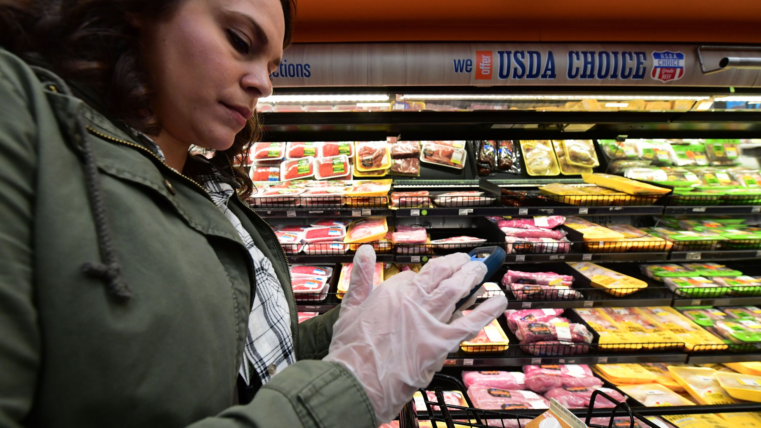 Instacart employee Monica Ortega wears gloves while using her cellphone to check orders while picking up groceries from a supermarket for delivery on March 19, 2020, in North Hollywood. (FREDERIC J. BROWN/AFP via Getty Images)