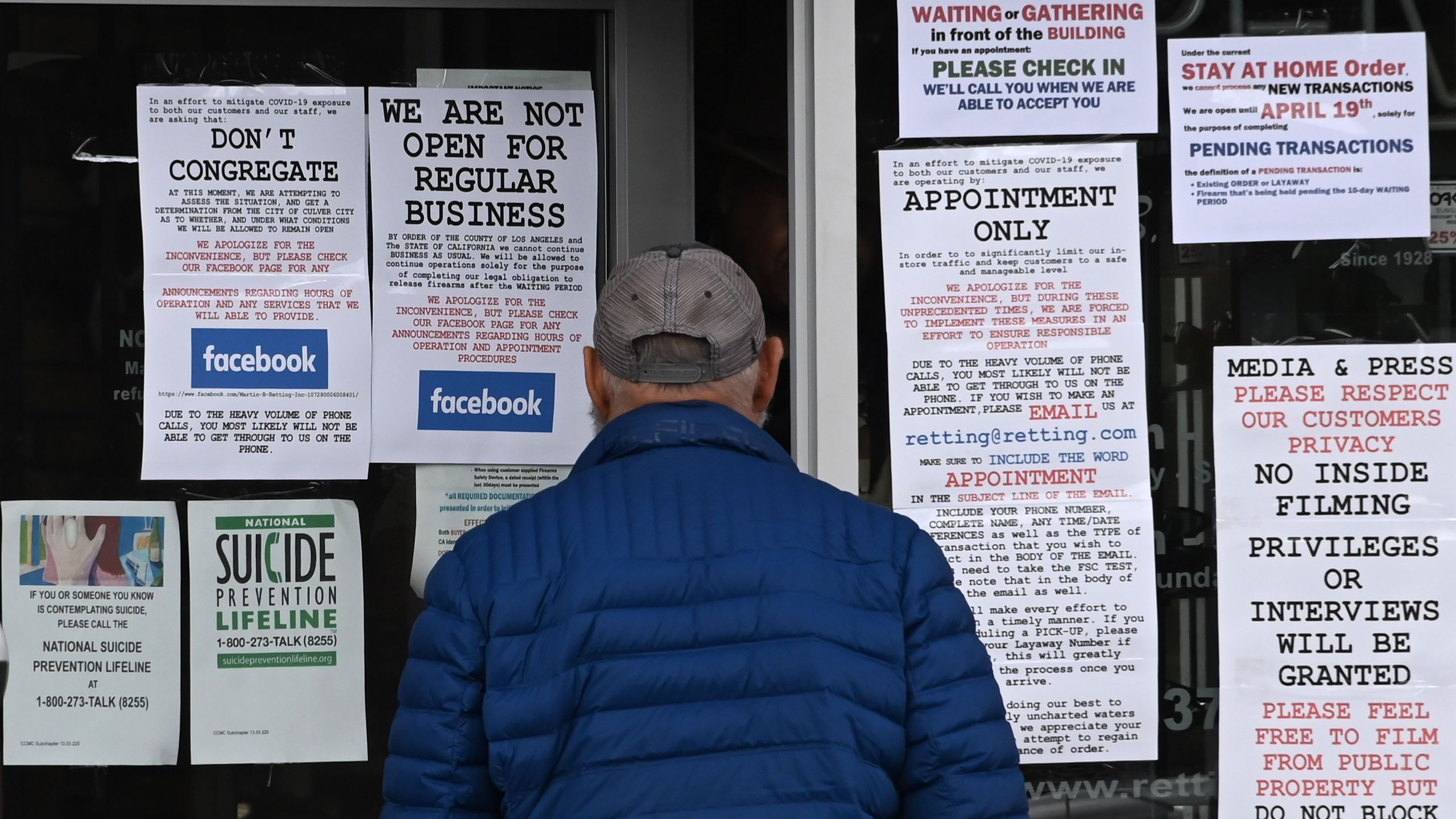 A man reads signs on the entrance to Martin B. Retting gun shop in Culver City on March 24, 2020. (Robyn Beck / AFP / Getty Images)