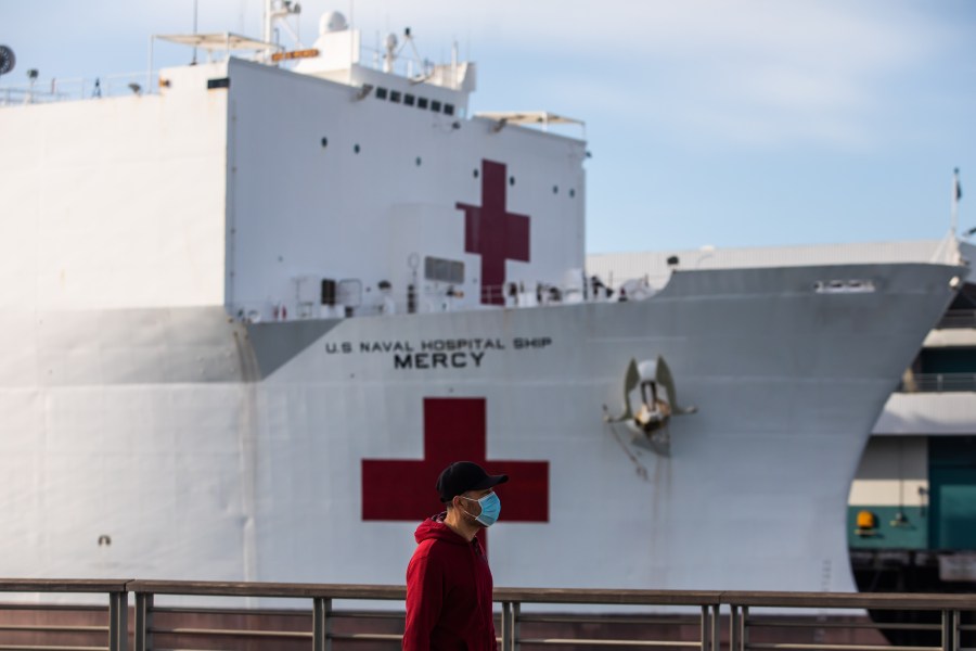 A man in a face mask walks past the U.S. Navy hospital ship, the USNS Mercy, on March 28, 2020, at the Port of Los Angeles in San Pedro. (Apu Gomes/AFP via Getty Images)