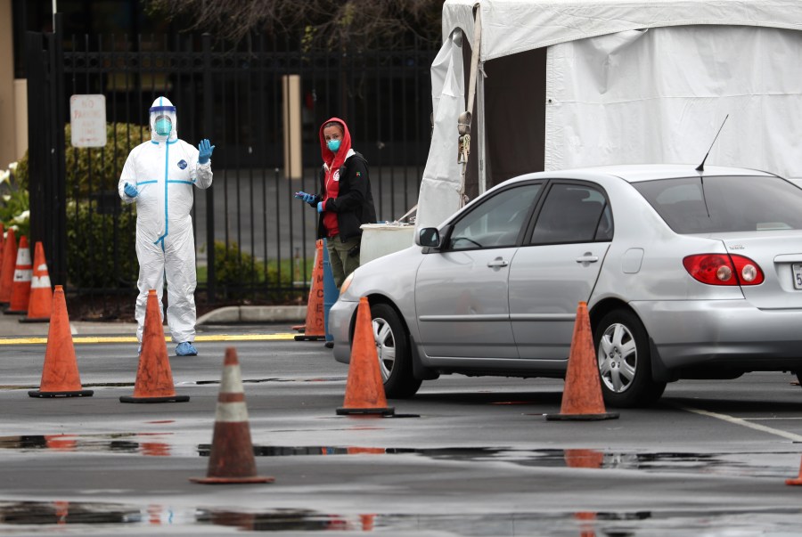 A medical worker guides a car that is going through a coronavirus drive-thru test clinic at the San Mateo County Event Center on March 16, 2020 in San Mateo, California. (Justin Sullivan/Getty Images)