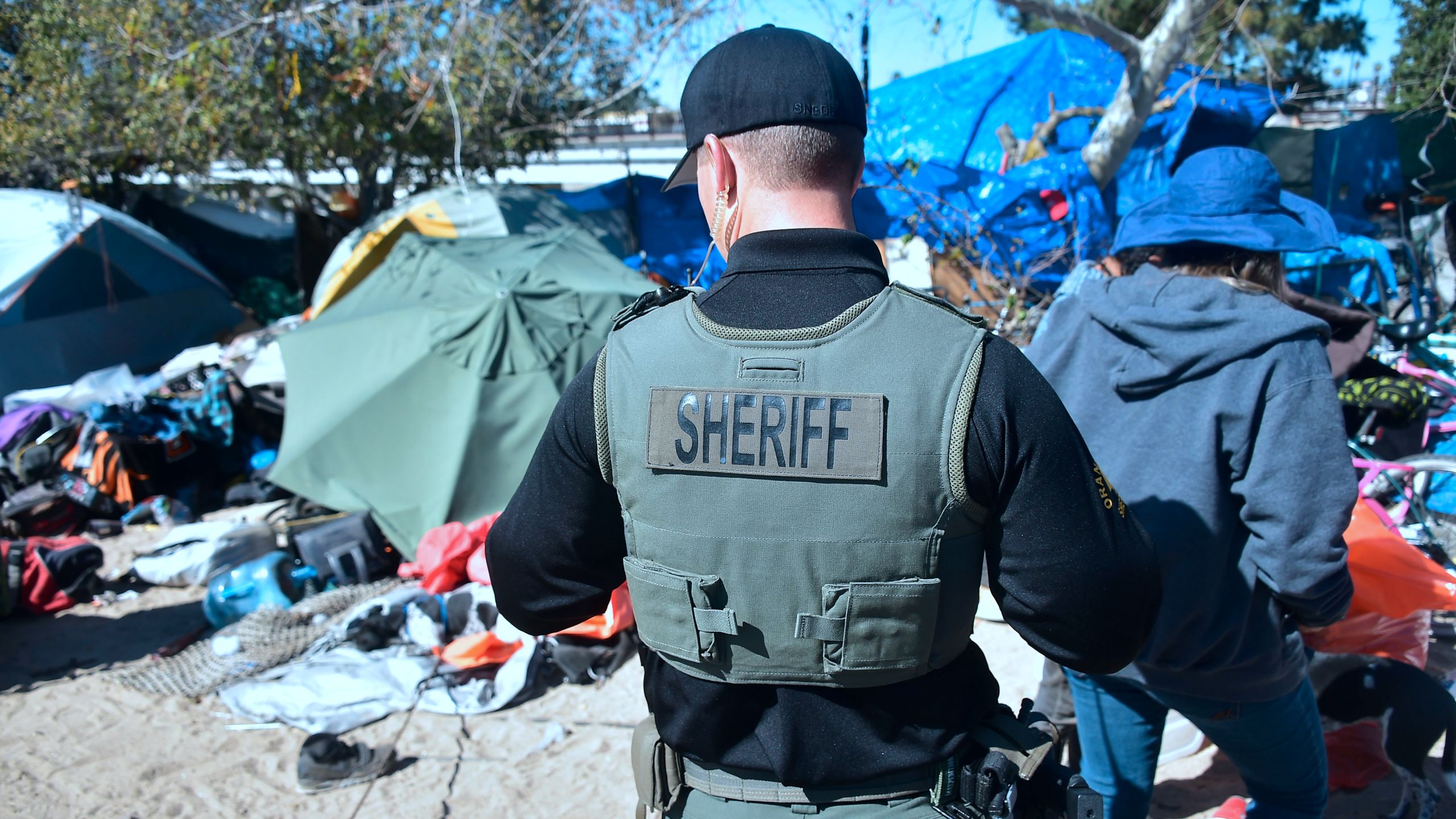 A deputy walks through a homeless encampment beside the Santa Ana River in Anaheim on Feb. 20, 2018.(Frederic J. Brown/ AFP via Getty Images)