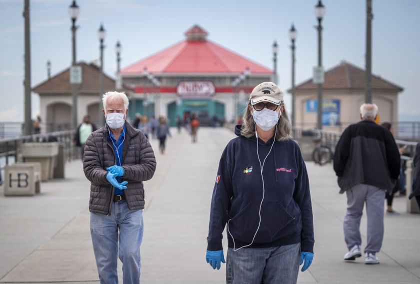 A couple in their 70s wear masks as they return from a walk on the Huntington Beach pier amid coronavirus restrictions. (Allen J. Schaben / Los Angeles Times)