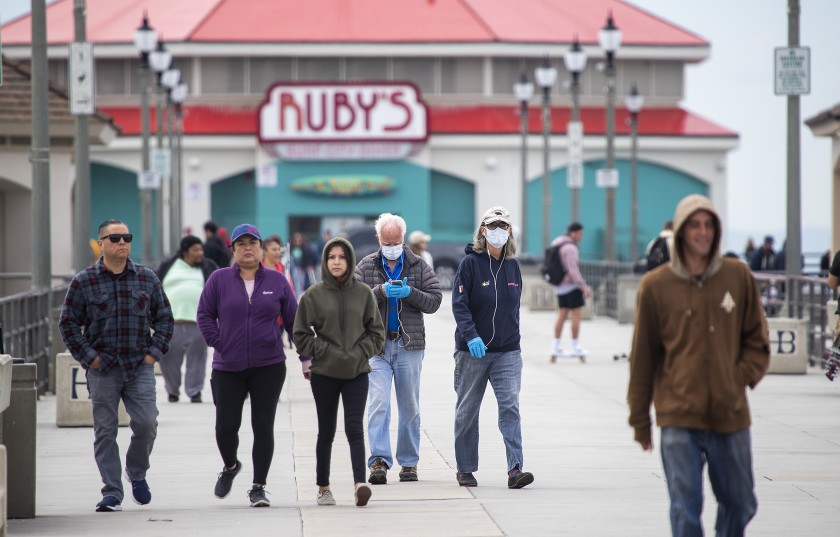 Beachgoers wear protective masks on March 18, 2020, as they return from a walk on the Huntington Beach pier.(Allen J. Schaben / Los Angeles Times)