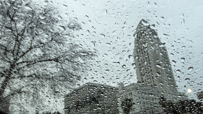 Los Angeles City Hall is pictured from behind glass covered in droplets on a rainy day in March 2020. (Credit: Los Angeles Times)