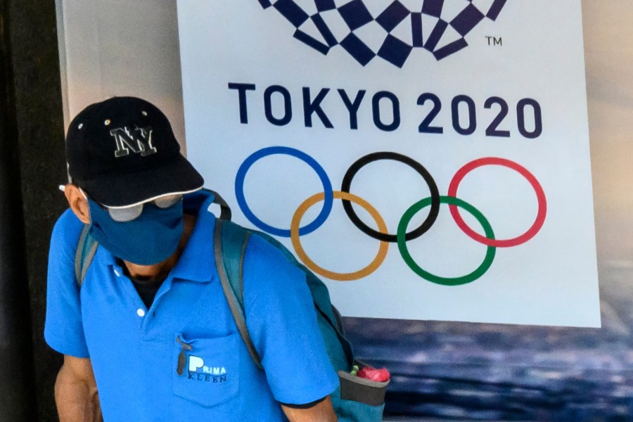 A man, wearing a face mask as a preventive measure against the spread of the COVID-19 novel coronavirus, sits at a bus stop in front of an advertisement for the Tokyo 2020 Summer Olympics Games in Bangkok on March 23, 2020. (MLADEN ANTONOV/AFP via Getty Images)