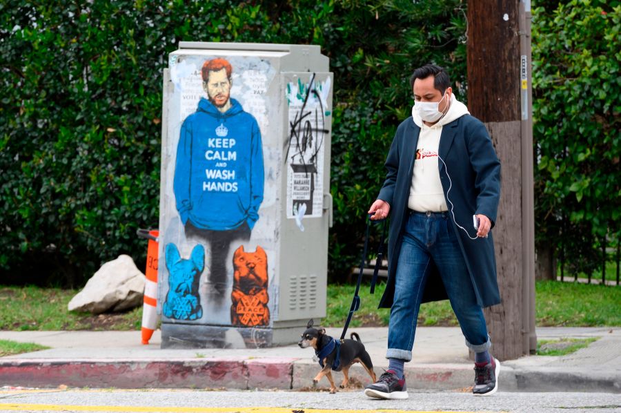 People walk past a painting of Prince Harry wearing a hoodie reading "Keep Calm and Wash Your Hands," on April 7, 2020, during the coronavirus pandemic in Los Angeles. (ROBYN BECK/AFP via Getty Images)