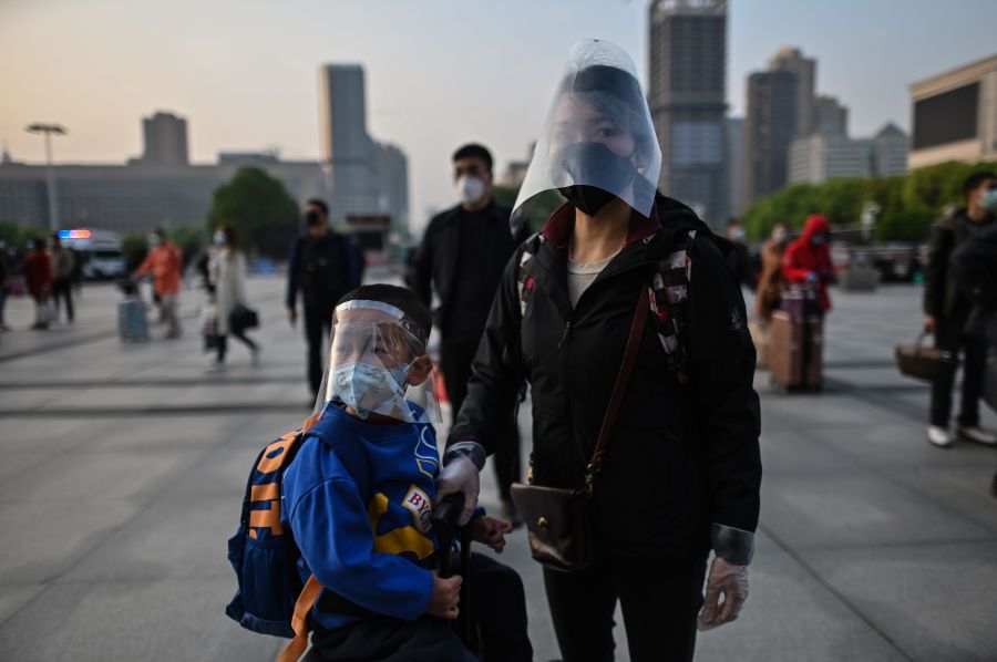 A boy wearing a face shield on top of a face mask waits with his mother to board one of the first trains leaving Wuhan after an outbound travel ban was lifted, at the Hankou railway station in Wuhan in China's central Hubei province early on April 8, 2020. (HECTOR RETAMAL/AFP via Getty Images)