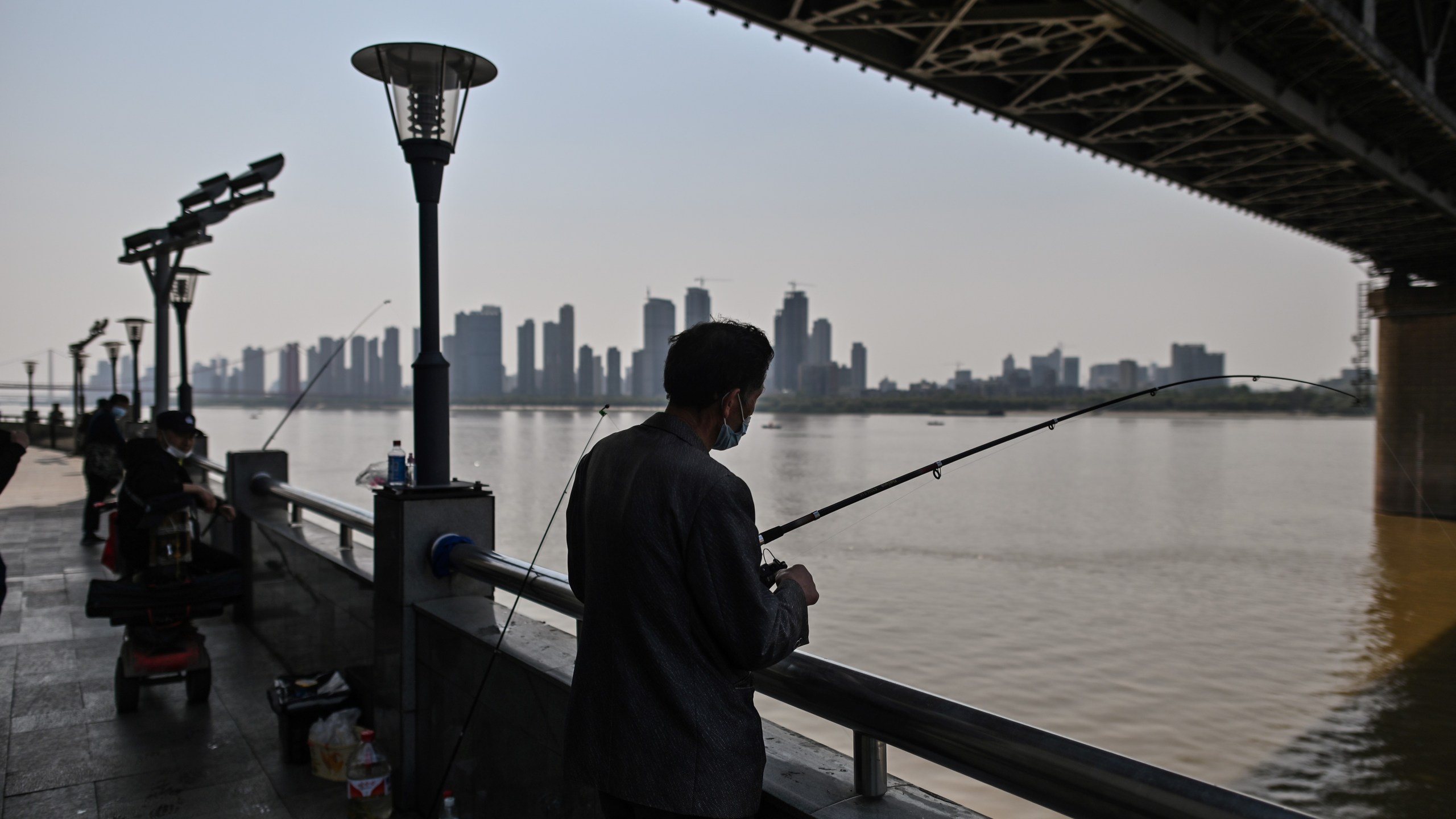 A man wearing a face mask fishes next to Wuhan Bridge in Yangtze River in Wuhan, China, on April 9, 2020. (HECTOR RETAMAL/AFP via Getty Images)