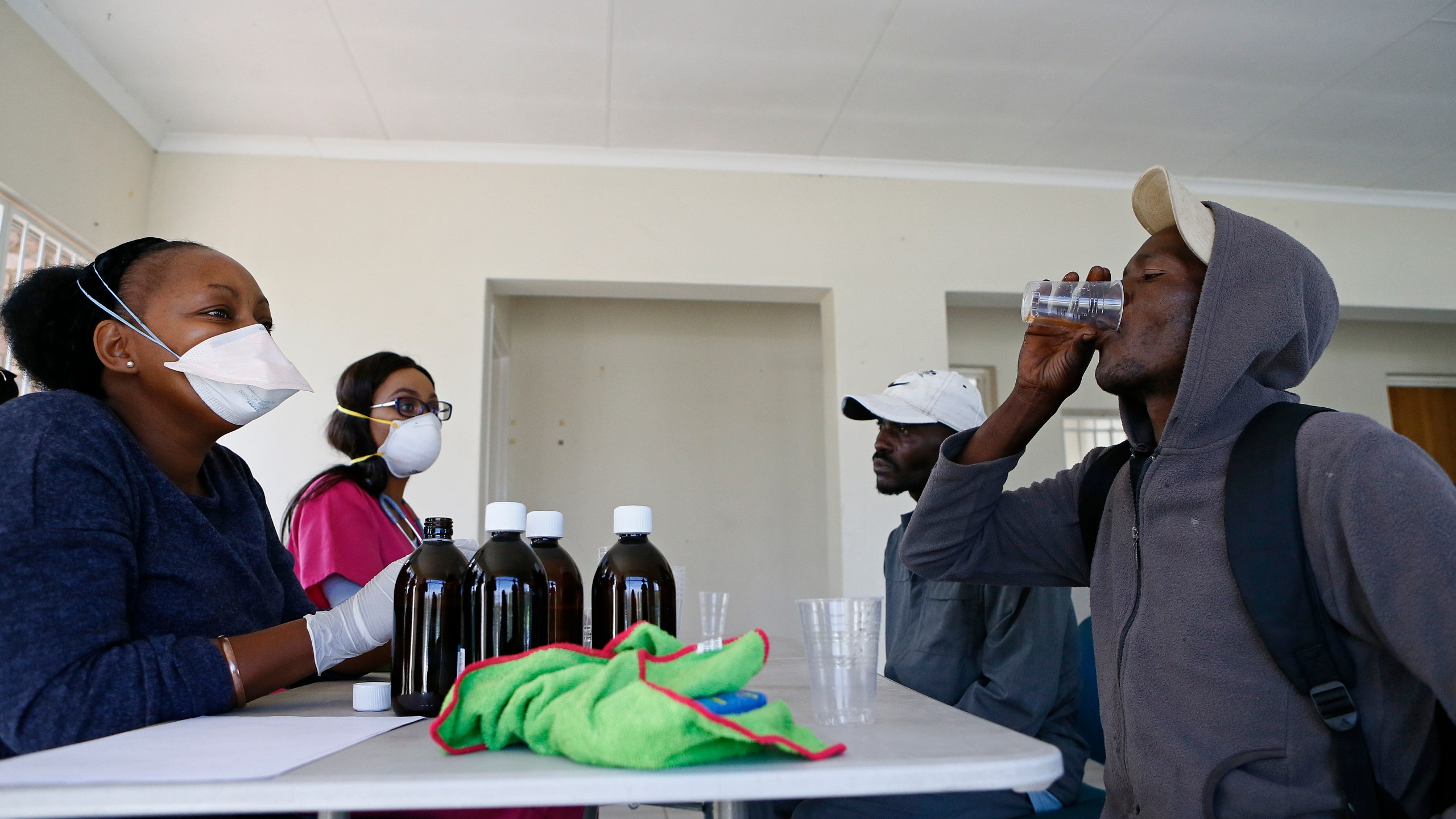 Health professionals look on as a homeless man drinks the Methadone Oral Solution, provided as an effort to care for drug-dependent people, at a shelter at the Lyttelton Sports Centre in Pretoria on April 16, 2020. The building is a temporary shelter being provided for homeless people amid the COVID-19 pandemic in South Africa. (Phill Magakoe / AFP via Getty Images)