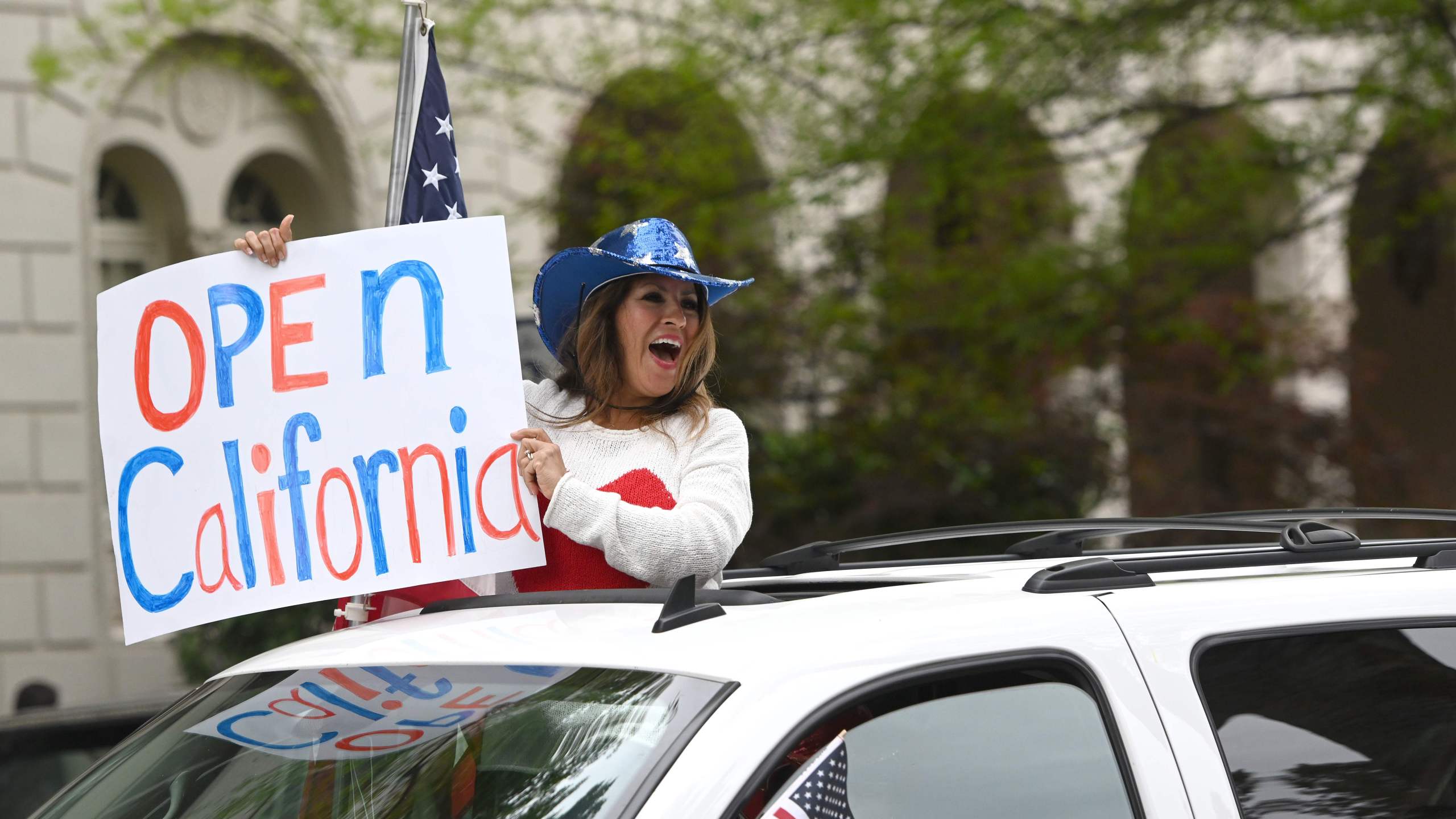 A woman holds out a sign calling for California to open as hundreds of people gather to protest the lockdown in spite of shelter-in-place rules at California's state capitol building in Sacramento on April 20, 2020.(JOSH EDELSON/AFP via Getty Images)