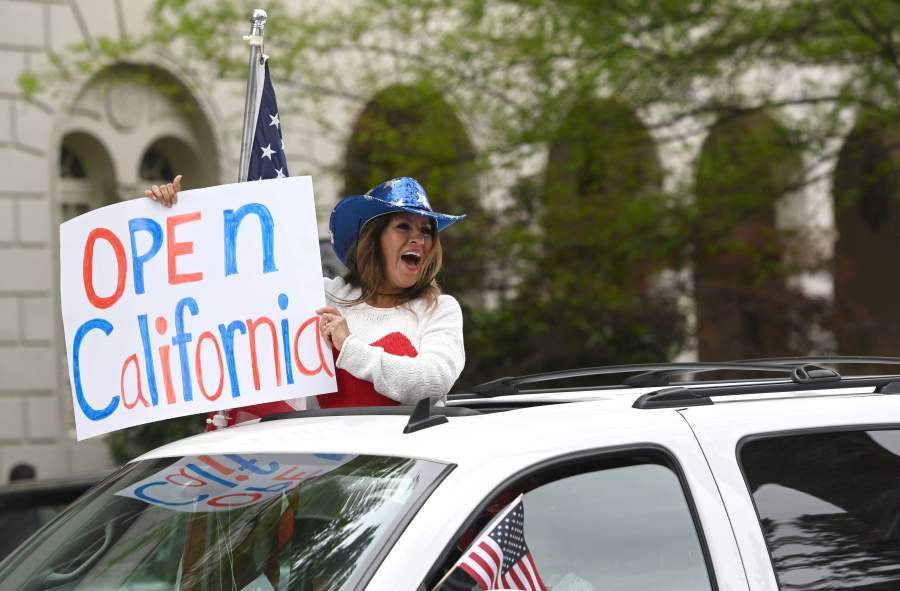 A woman holds out a sign calling for California to open as hundreds of people gather to protest the lockdown in spite of shelter-in-place rules at California's state capitol building in Sacramento on April 20, 2020.(JOSH EDELSON/AFP via Getty Images)