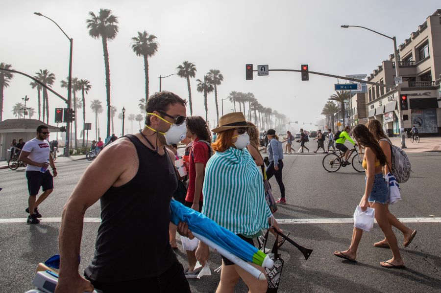 People cross the street, some wearing masks, in Huntington Beach amid the novel coronavirus pandemic on April 25, 2020. (Apu Gomes / AFP / Getty Images)