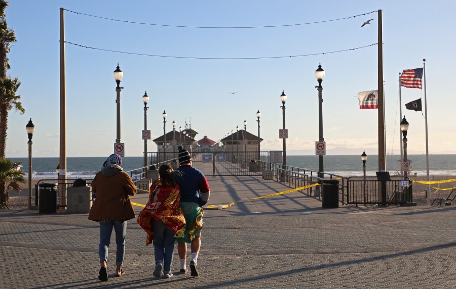 People stand in front of the closed Huntington Beach Pier on March 24, 2020, in Huntington Beach. Gov. Gavin Newsom at the time issued a “soft closure” of state parks in the hopes of slowing the spread of COVID-19. (Michael Heiman/Getty Images)