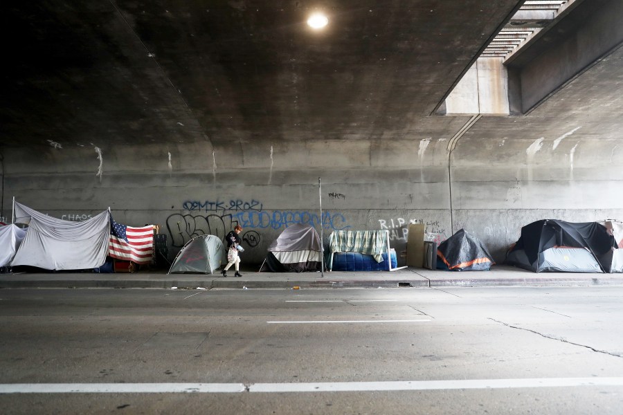 A woman walks past a homeless encampment beneath an overpass in Los Angeles, with an American flag displayed, amid the coronavirus pandemic on April 4, 2020. (Mario Tama / Getty Images)