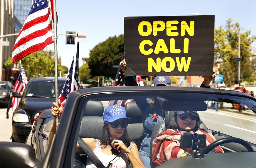 A group of protesters, including Alma Villanueva, left, and Gigi Wilcox, right, stage a vehicle caravan protest April 22 in downtown Los Angeles calling on state and local officials to reopen the economy.(Christina House / Los Angeles Times)