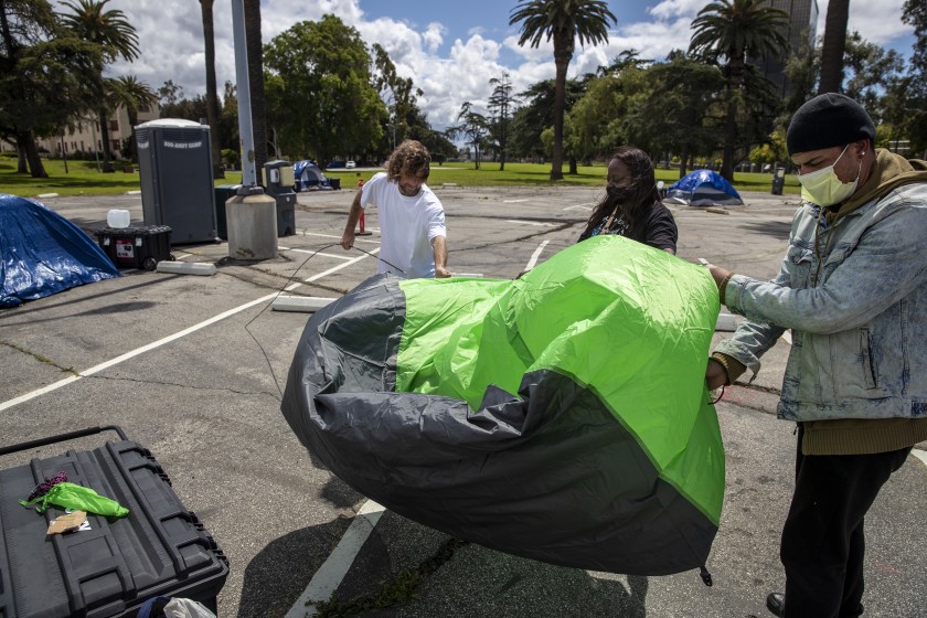 VA community outreach worker Michelle O’Neal, center, helps homeless veterans Larry McNearney, left, and Timothy Cornejo, right, set up Cornejo’s tent in a VA parking lot in Los Angeles.(Brian van der Brug / Los Angeles Times)