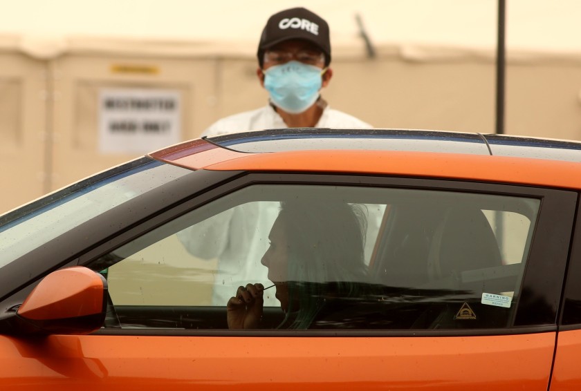 A woman takes a self-administered COVID-19 test, under the instruction of a health worker, at a drive-up testing site outside Jackie Robinson Stadium off the UCLA campus.(Genaro Molina / Los Angeles Times)