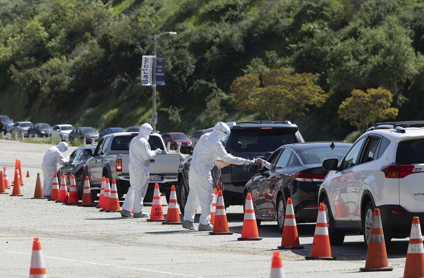 Members of the Los Angeles Fire Department wear protective gear as they hand out coronavirus test kits in a parking lot on Stadium Way, near Dodger Stadium. (Mel Melcon / Los Angeles Times)