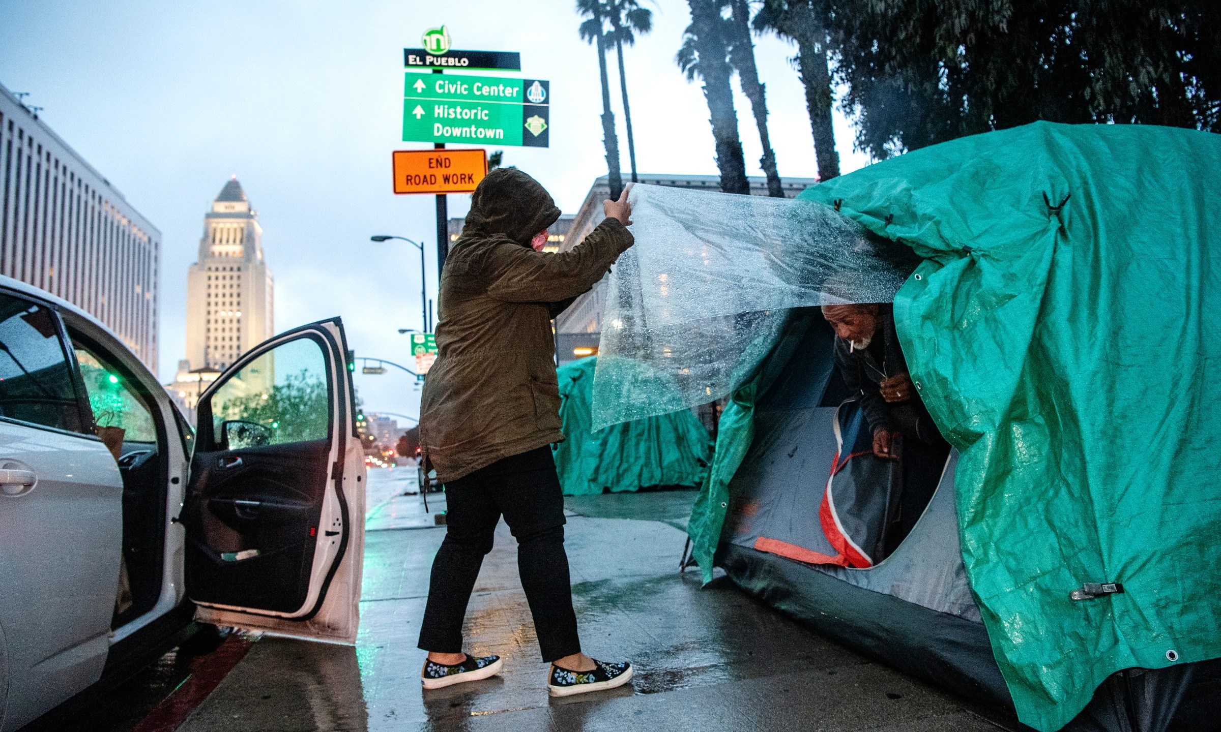 Melissa Acedera distributes meals and supplies to one of her contacts, Harvey, on Olvera Street on a rainy evening in downtown Los Angeles. The COVID-19 pandemic and ensuing hoarding have disrupted food supply lines to shelters and organizations that feed L.A.'s homeless residents.(Mariah Tauger / Los Angeles Times)