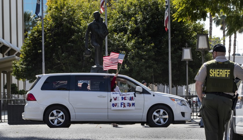 A demonstrator waves an American flag at a Riverside County sheriff’s deputy in 2020 while participating in a car rally to protest conditions in the county’s jails, which has endured a coronavirus outbreak.(Gina Ferazzi / Los Angeles Times)