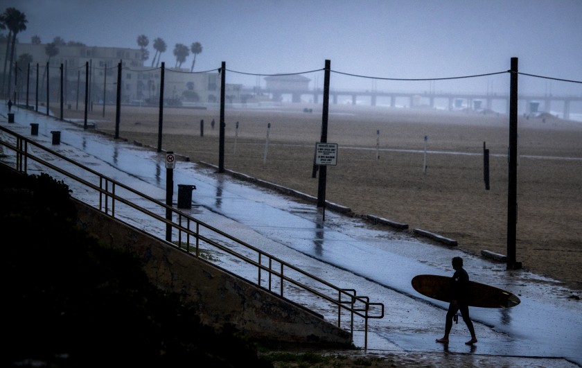 A surfer walks on an empty bike path amid steady rainfall in Huntington Beach in April 2020. (Allen J. Schaben / Los Angeles Times)