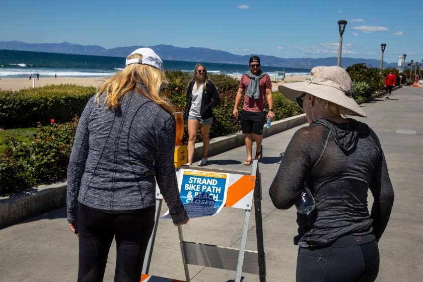 People stop to read a sign on the Strand in Manhattan Beach in March 2020 after officials closed all Los Angeles County beaches. (Jay L. Clendenin / Los Angeles Times)