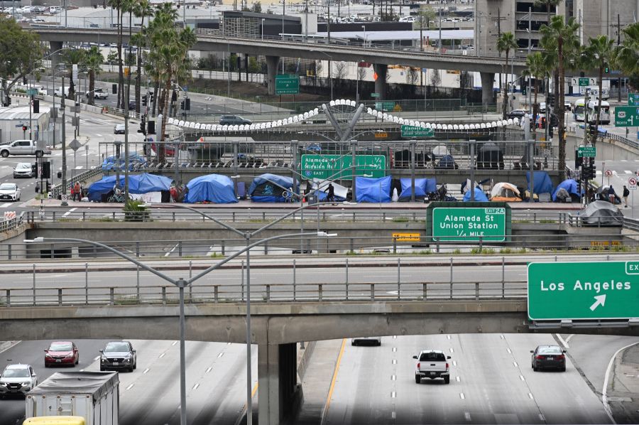 A man rides a bicycle in front of a row of homeless tents above a freeway on April 7, 2020 in Los Angeles. (ROBYN BECK/AFP via Getty Images)