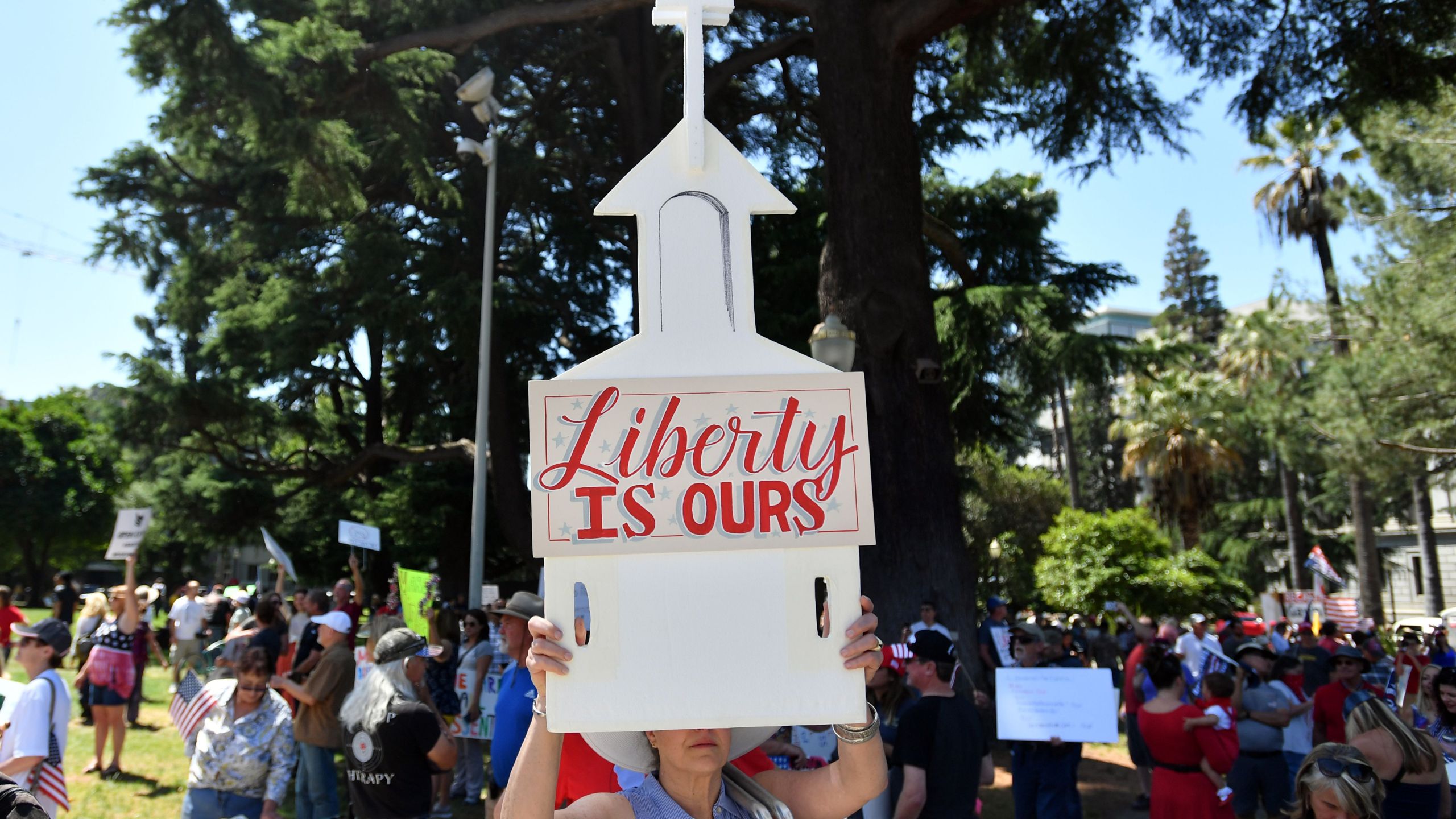 A woman holds up a sign depicting a church as hundreds of people gather to protest the stay-at-home orders outside the state capitol building in Sacramento on May 1, 2020. (JOSH EDELSON/AFP via Getty Images)