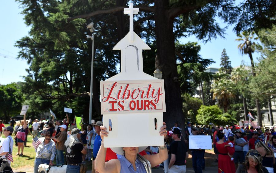 A woman holds up a sign depicting a church as hundreds of people gather to protest the stay-at-home orders outside the state capitol building in Sacramento on May 1, 2020. (JOSH EDELSON/AFP via Getty Images)